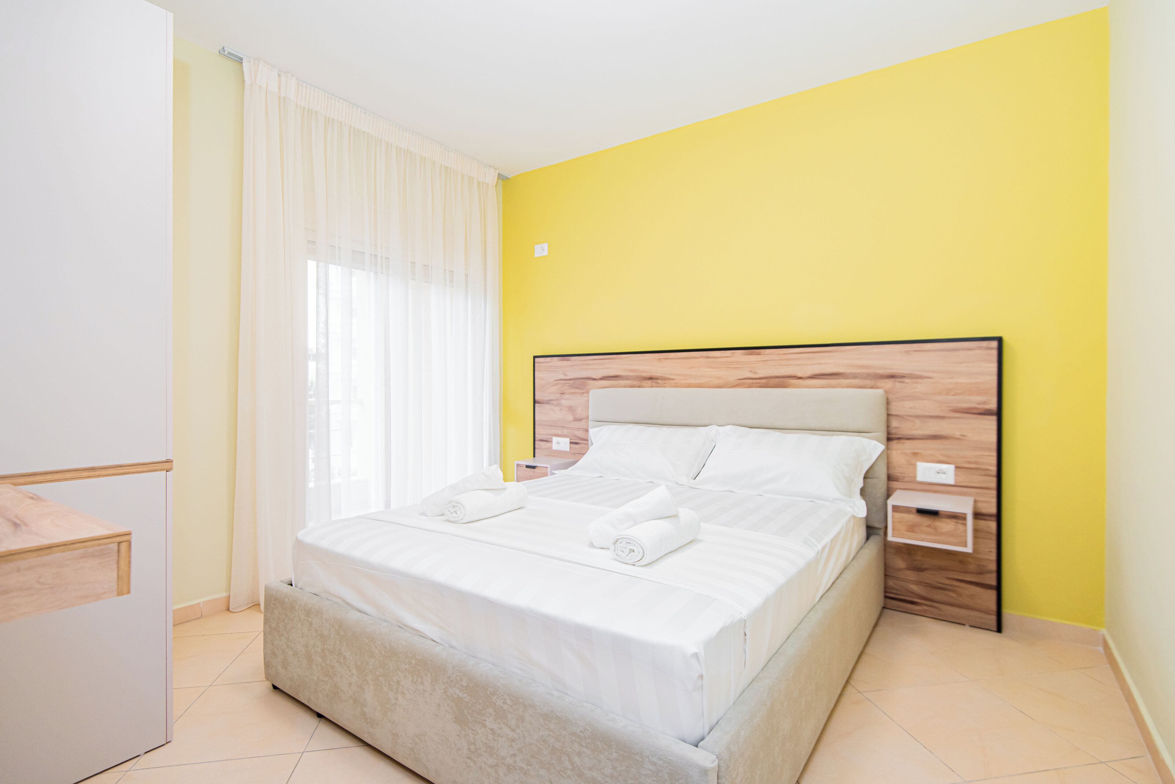 A bedroom with a bed, a bedside table, a nightstand, and a window with curtains.