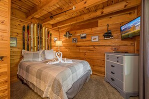 Ein Schlafzimmer in einer Holzhütte mit einem Bett, Skiern an der Wand, einem Schminktisch und einem Fernseher.