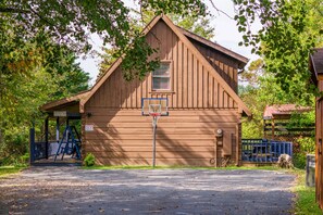 Ein Holzgebäude mit Basketballkorb, einer überdachten Veranda und einem kleinen Garten.