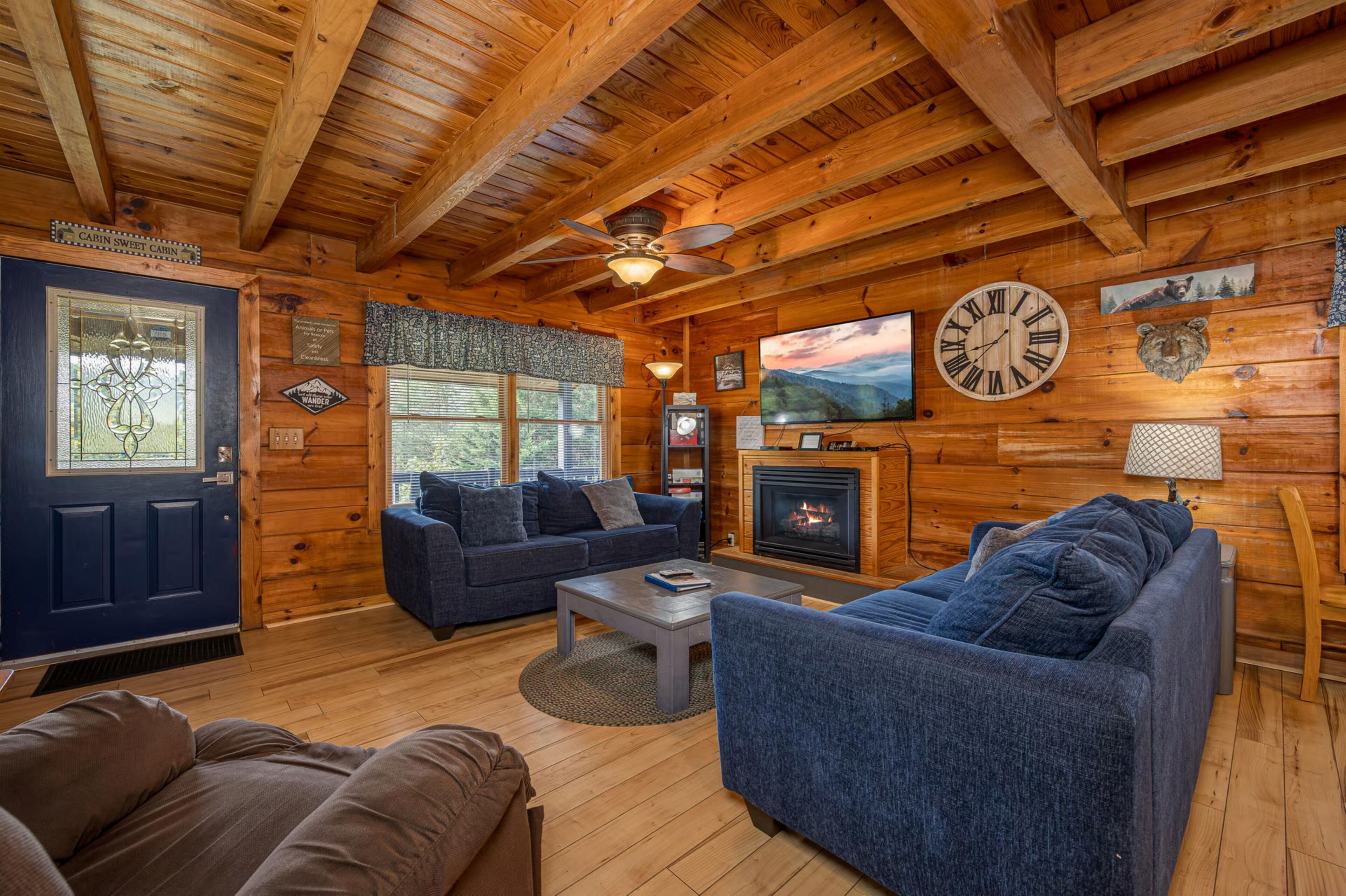 A log cabin interior with a fireplace, a large clock, and a television.