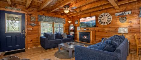 A log cabin interior with a fireplace, a large clock, and a television.