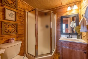 Bathroom features a glass-enclosed shower, wooden vanity with sink and mirror, and a toilet with a towel hanging nearby.