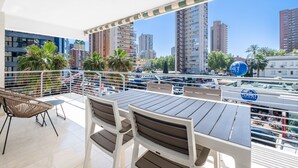 A balcony with a table and chairs, overlooking a cityscape with tall buildings and palm trees. - Niza 2-A Apartment Levante Beach (Benidorm)