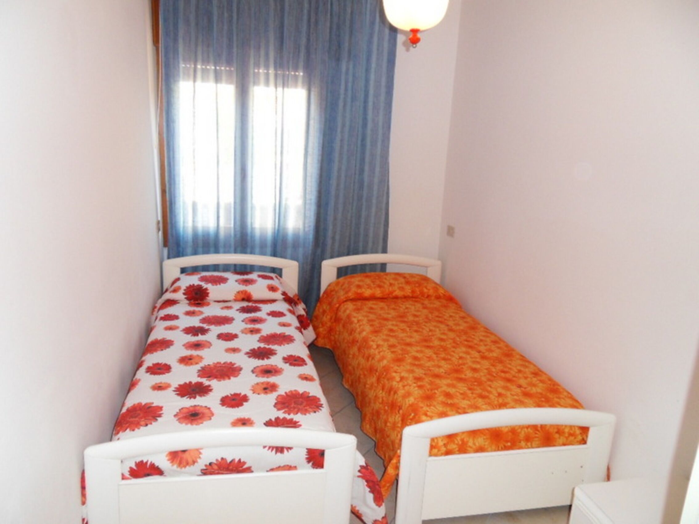 Una habitación pequeña con dos camas individuales, una ventana con cortinas azules y una pared blanca.