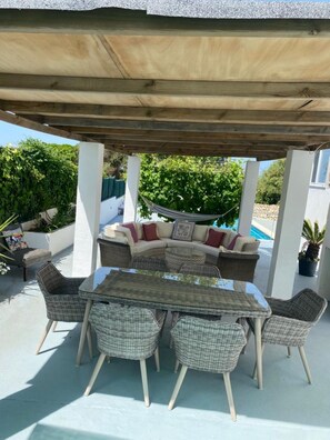 Eine Terrasse im Freien mit überdachter Sitzgruppe, einem Tisch und Stühlen.