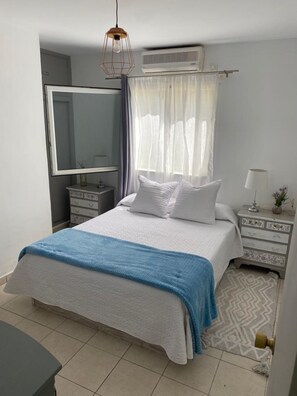 Ein Schlafzimmer mit Bett, Nachttisch, Spiegel und Klimaanlage.