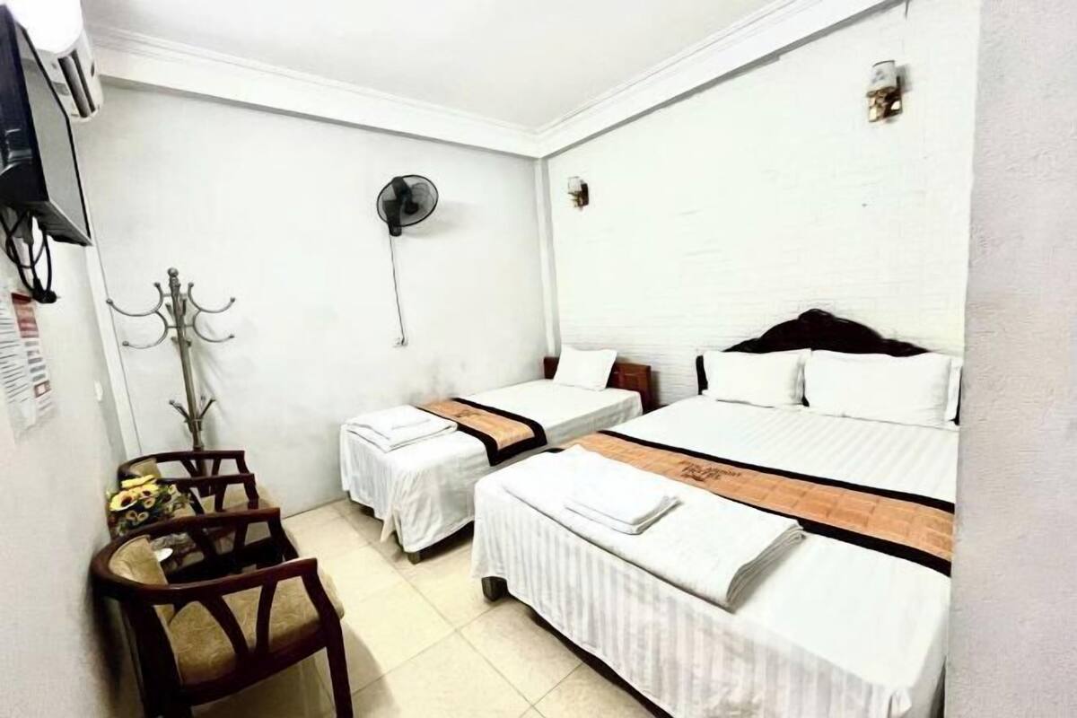 Habitación de hotel con dos camas, un escritorio, una silla, un ventilador y una lámpara fijada a la pared.