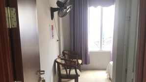 Un pasillo con puerta de madera, ventilador, una silla, cama y aire acondicionado.