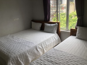 Un dormitorio con dos camas, una ventana con cortinas y vistas a la vegetación.