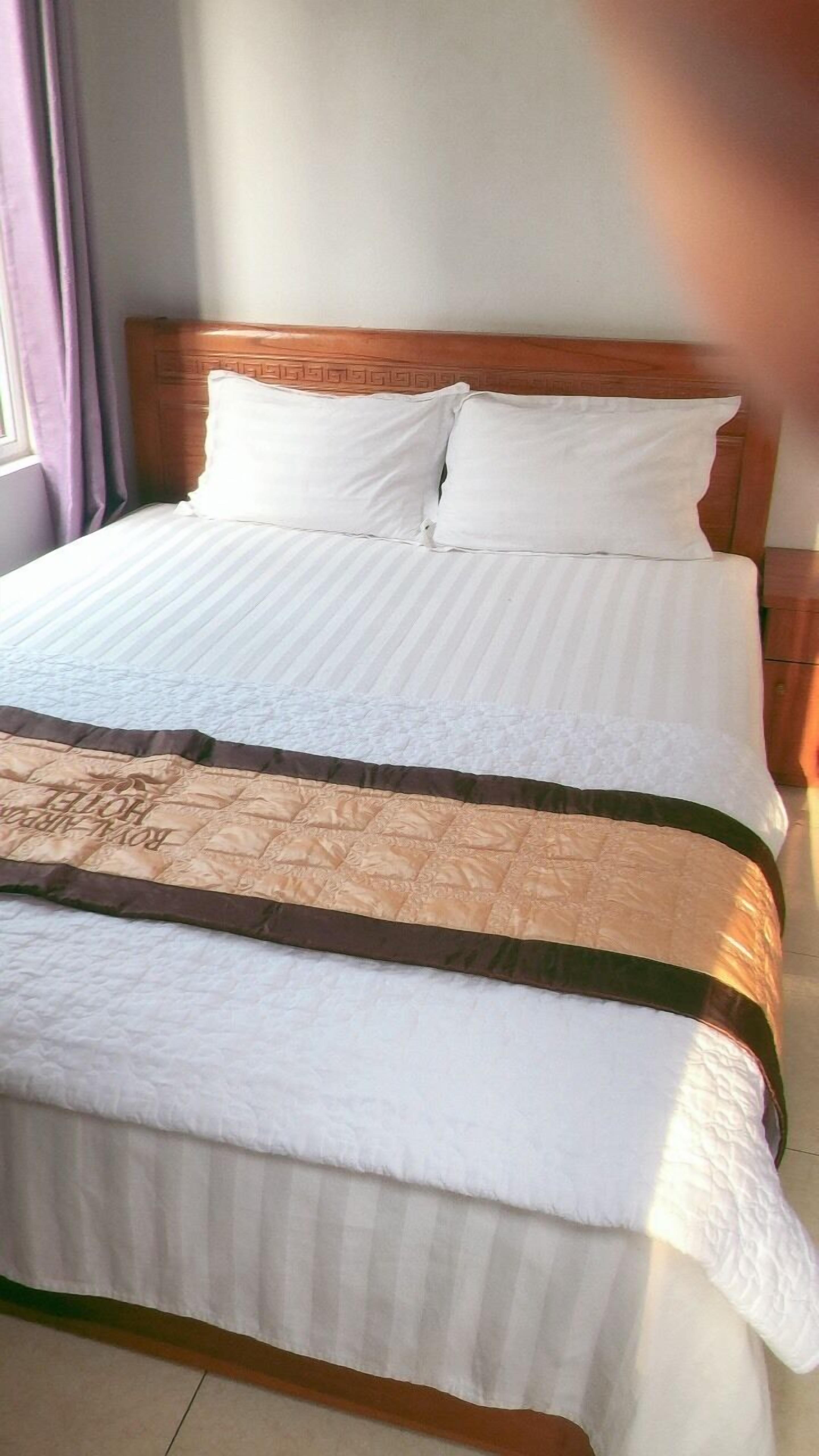 Un lit avec une tête de lit en bois, une literie blanche et une couverture marron.