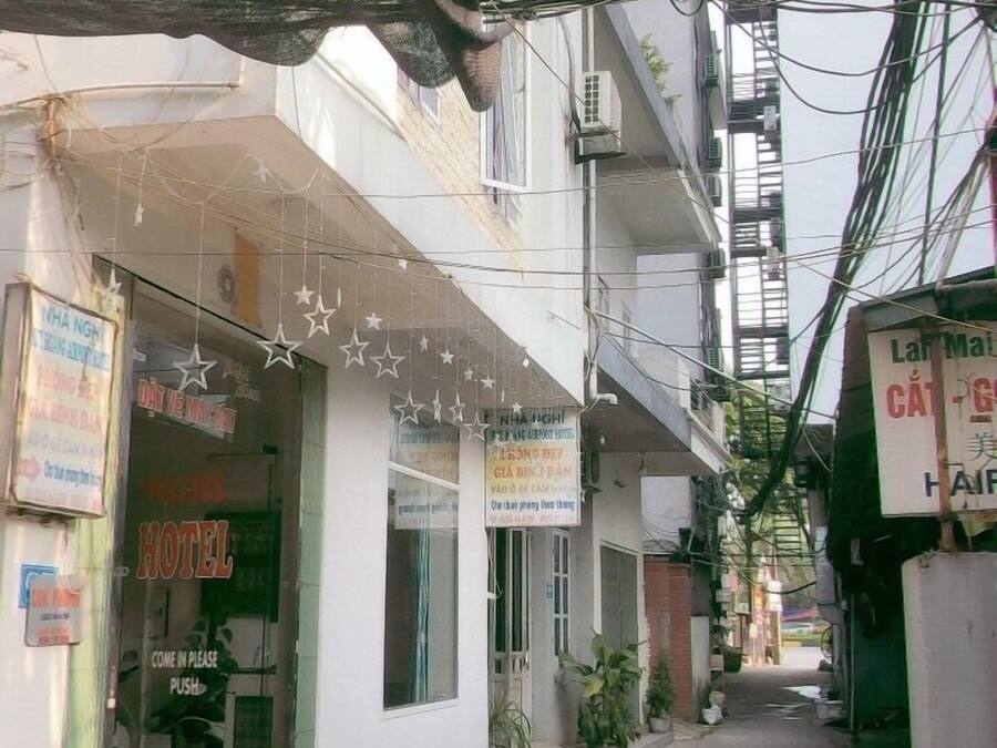 A narrow alley with a hotel on the left, a sign for a hair salon on the right, and various signs and wires overhead.