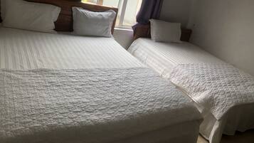 Une chambre avec deux lits, chacun doté de draps et d’oreillers blancs, et d’une tête de lit en bois.