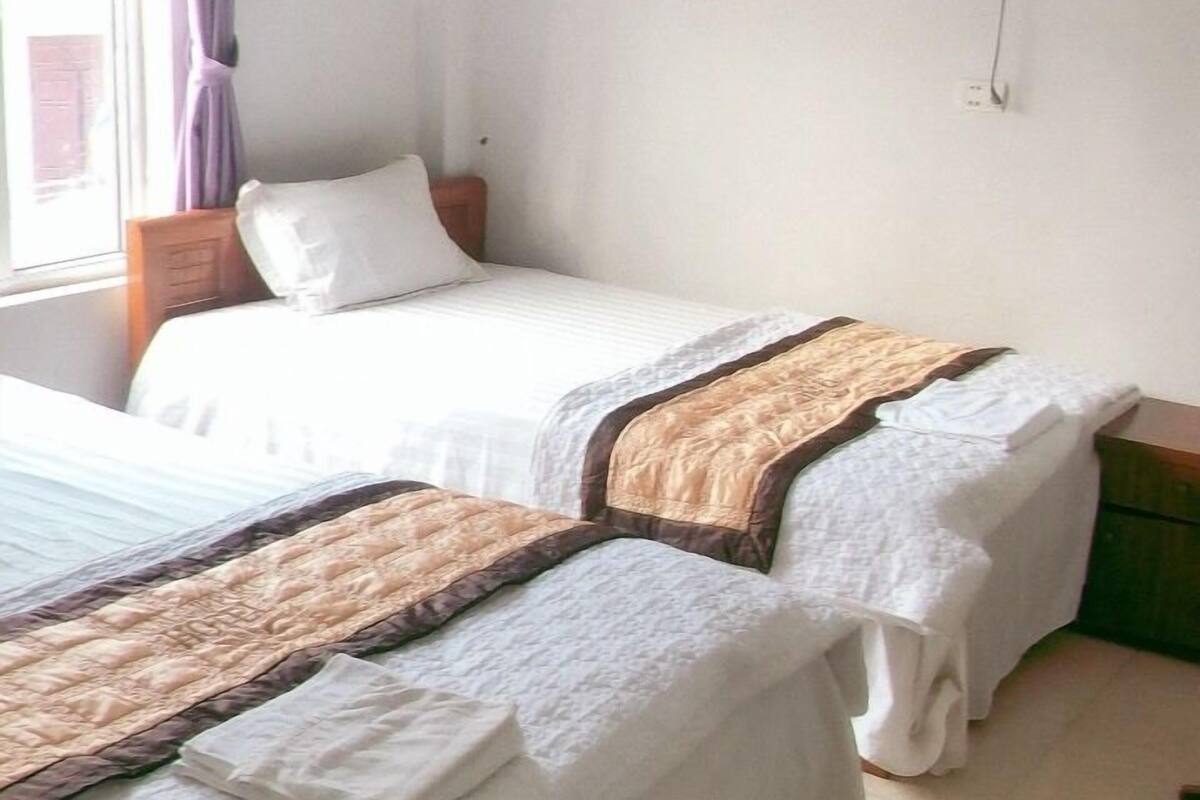 Una habitación con dos camas, una ventana con cortinas moradas, aire acondicionado de pared y un ventilador de techo.