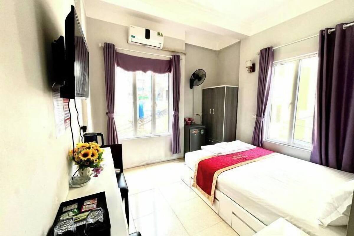 Una habitación de hotel con cama, escritorio con computadora, televisor, ventana con cortinas y equipo de aire acondicionado.