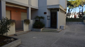 Un bâtiment moderne doté d’une entrée sécurisée par un portail, d’un petit jardin agrémenté de plantes et d’une cour dallée.