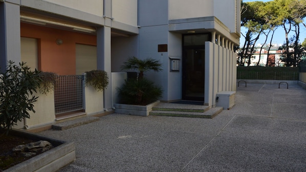 A modern building with a gated entrance, a small garden area with plants, and a paved courtyard.