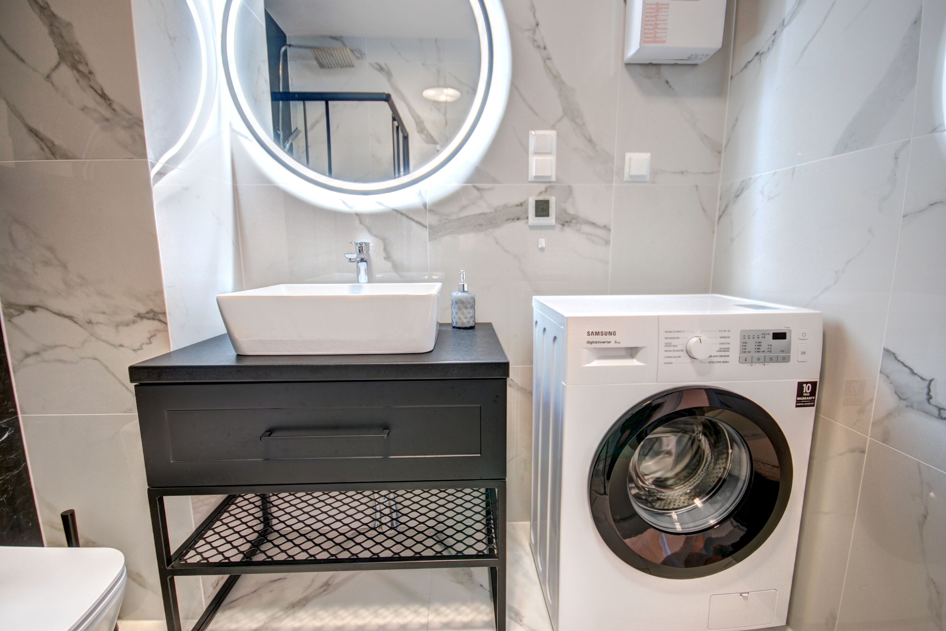 Ein modernes Badezimmer mit Waschbecken in Weiß, schwarzem Waschtisch und integrierter Waschmaschine.