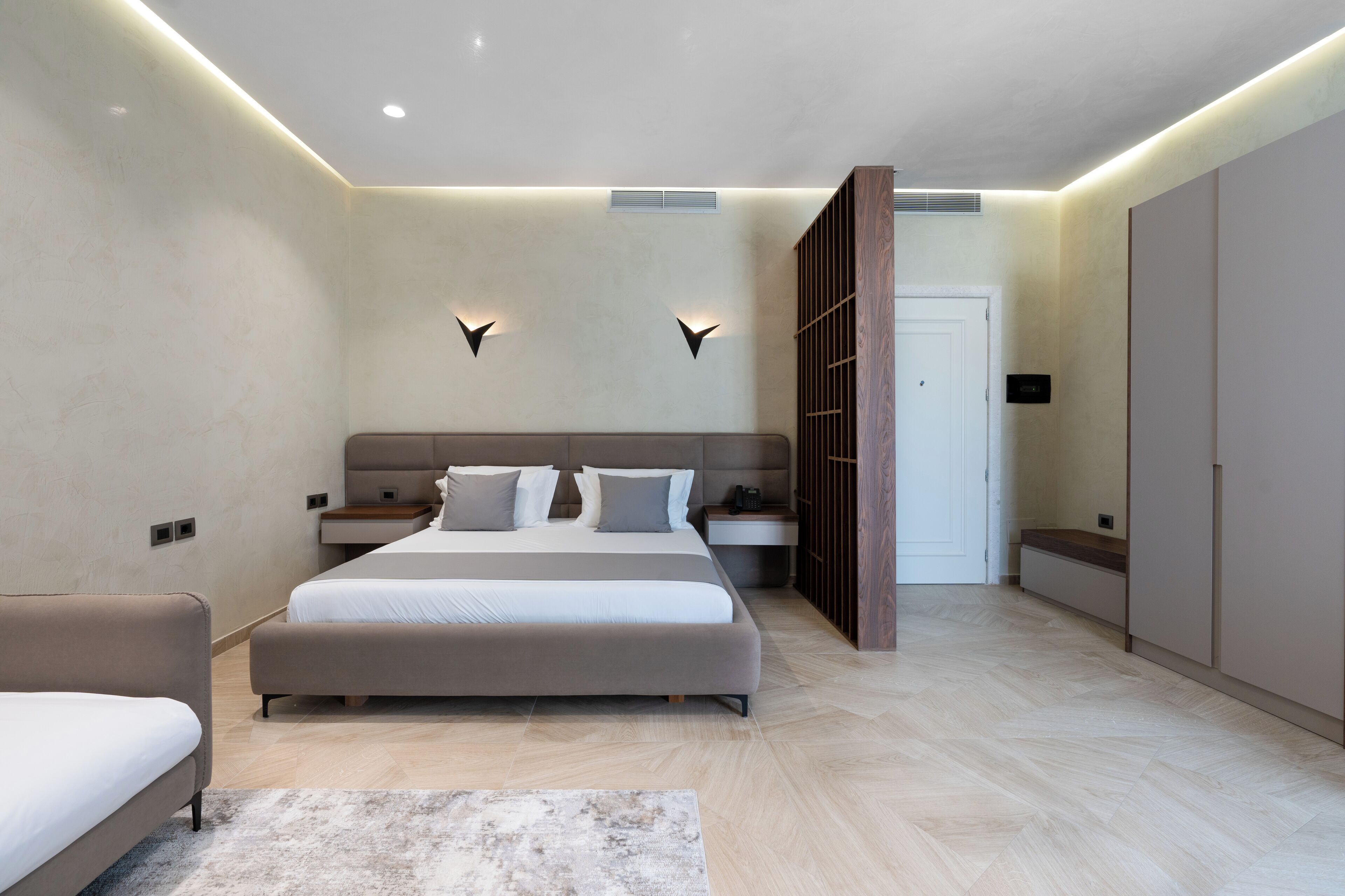 A modern bedroom with a large bed, bedside tables, a wardrobe, and a built-in bench.