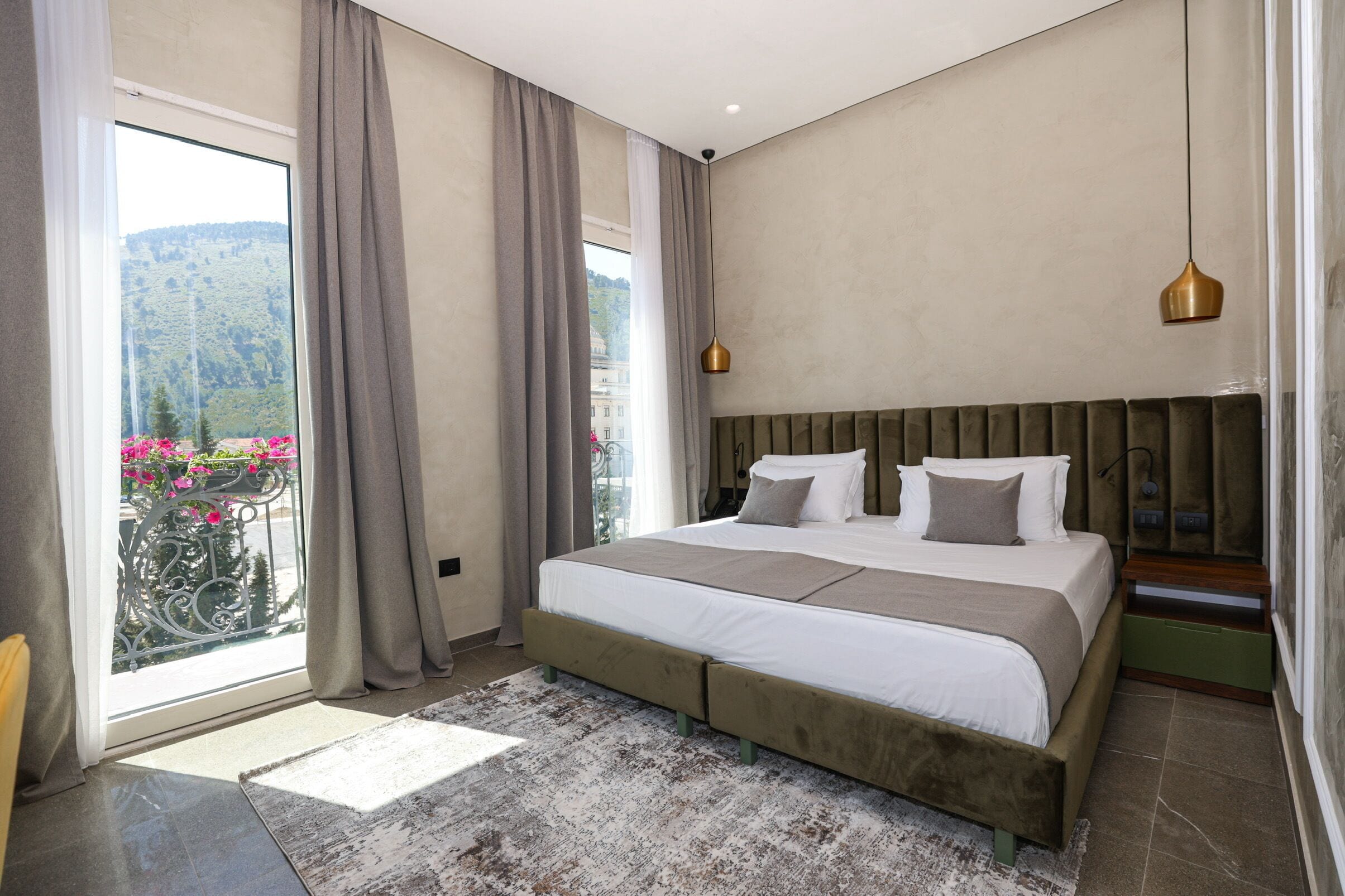 Un dormitorio con una cama grande, vistas a un balcón con flores y una lámpara colgante moderna.