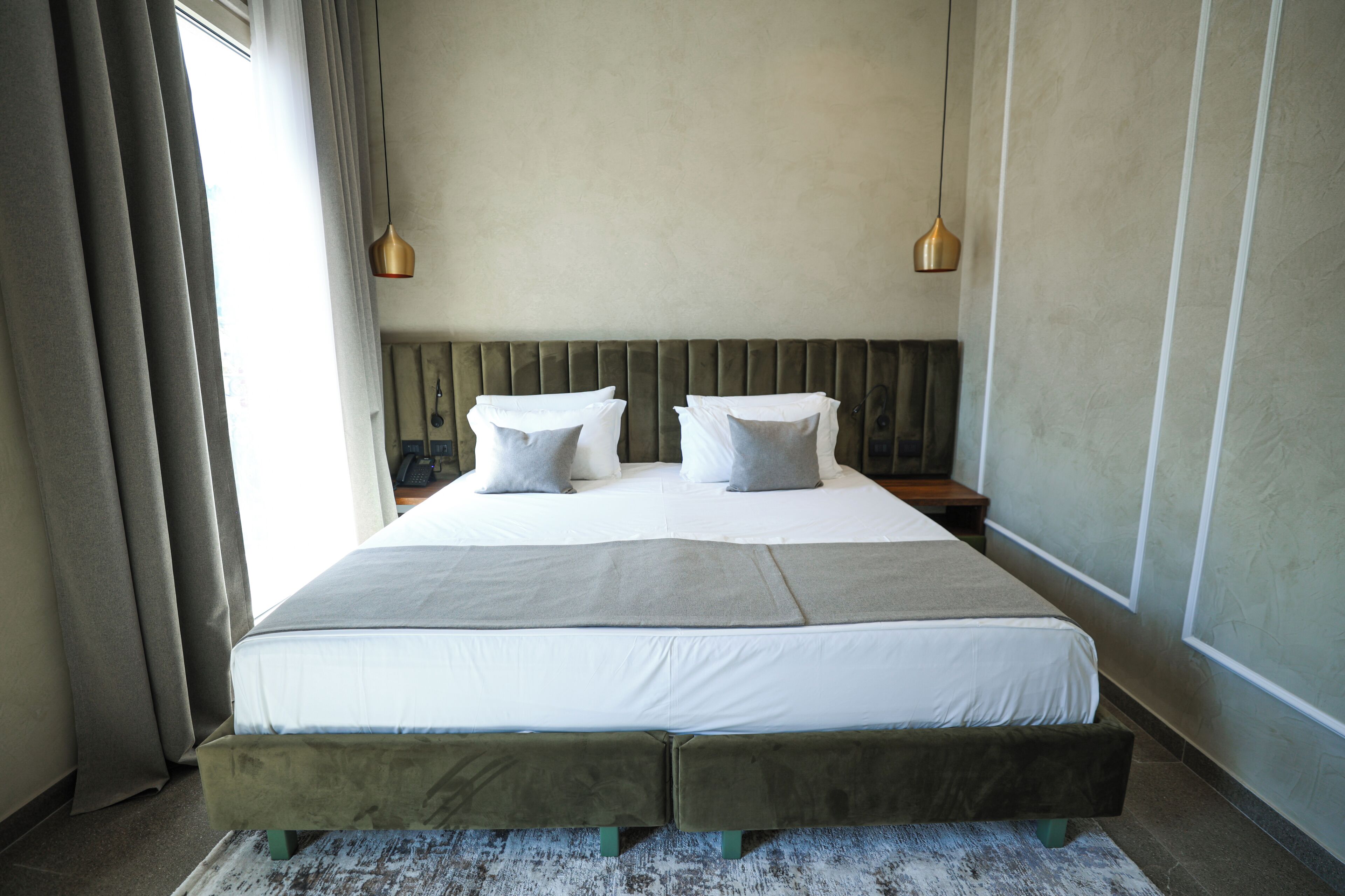 A neatly made bed with a headboard, two bedside tables, and two pendant lights.