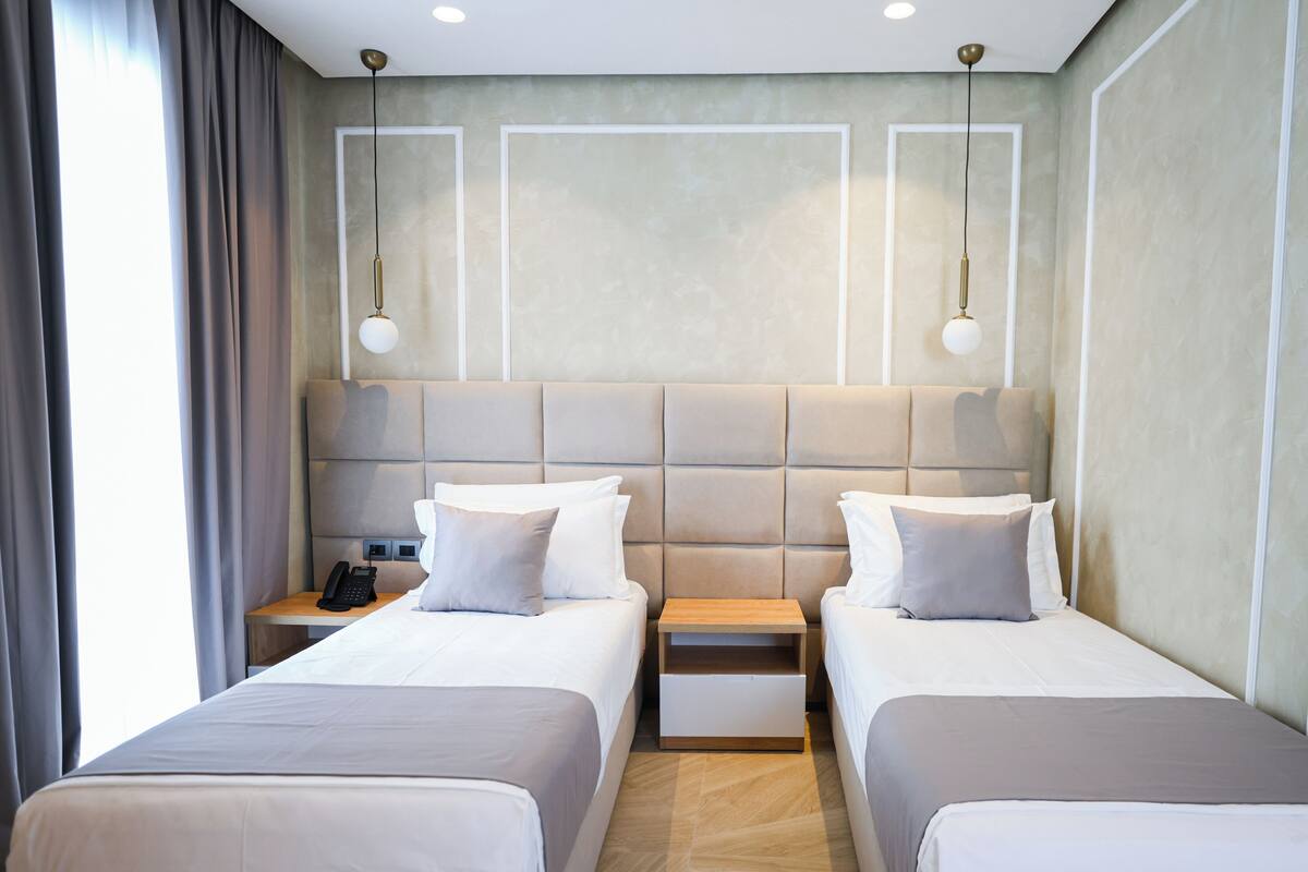 Habitación de hotel con dos camas, una mesita de noche con teléfono y una lámpara sobre las camas.