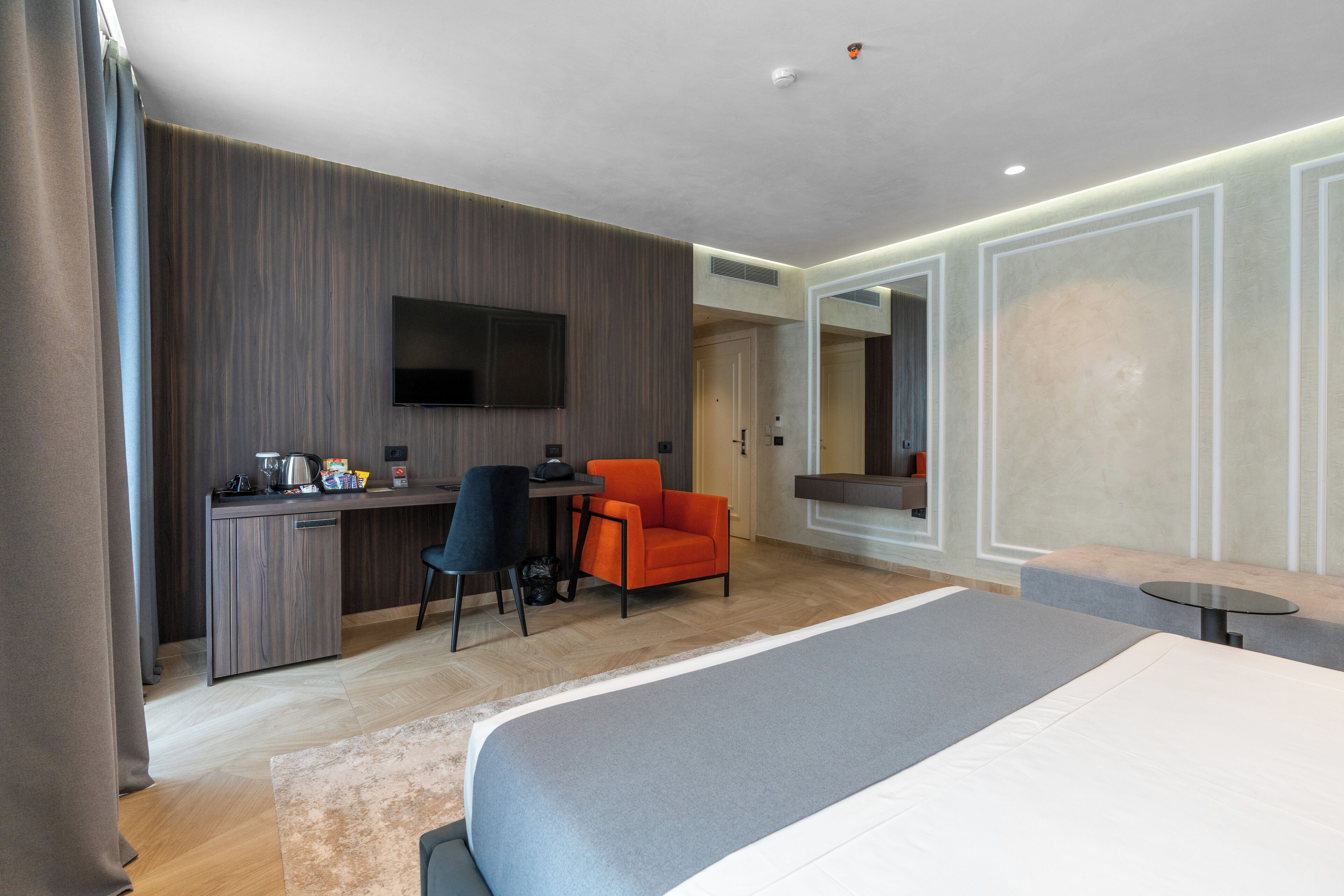 A modern hotel room with a large bed, a desk with a chair, a television, and a small table.
