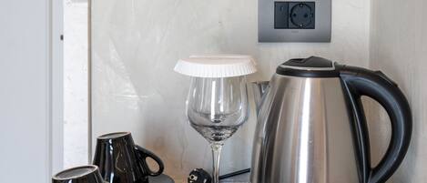 A coffee station with a kettle, cups, a glass, and coffee packets.