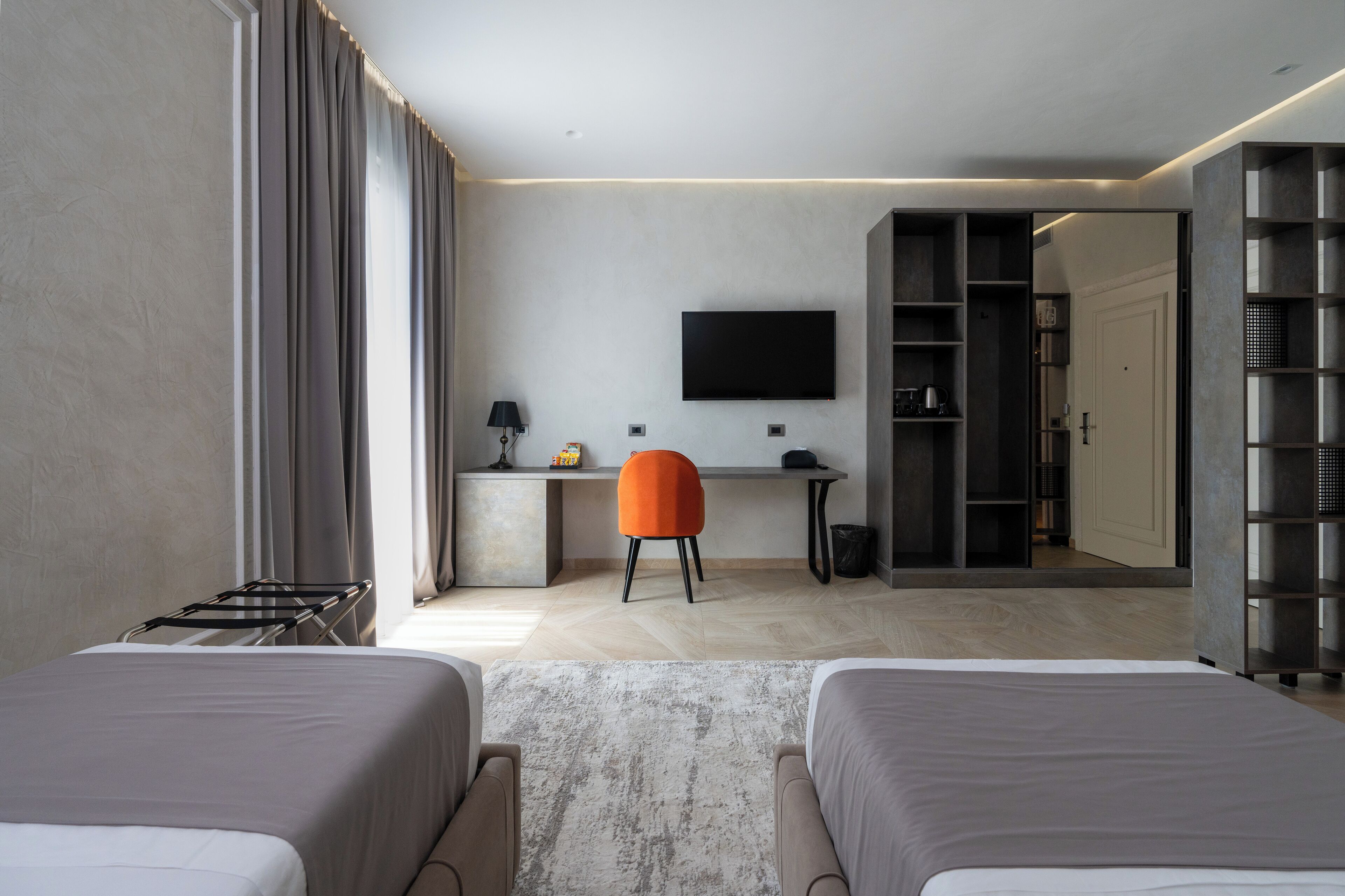 Una habitación de hotel moderna con dos camas, un escritorio, un televisor y un armario.