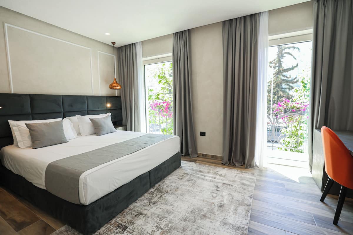 Un dormitorio moderno con una cama grande, cortinas grises y vistas a zonas verdes.