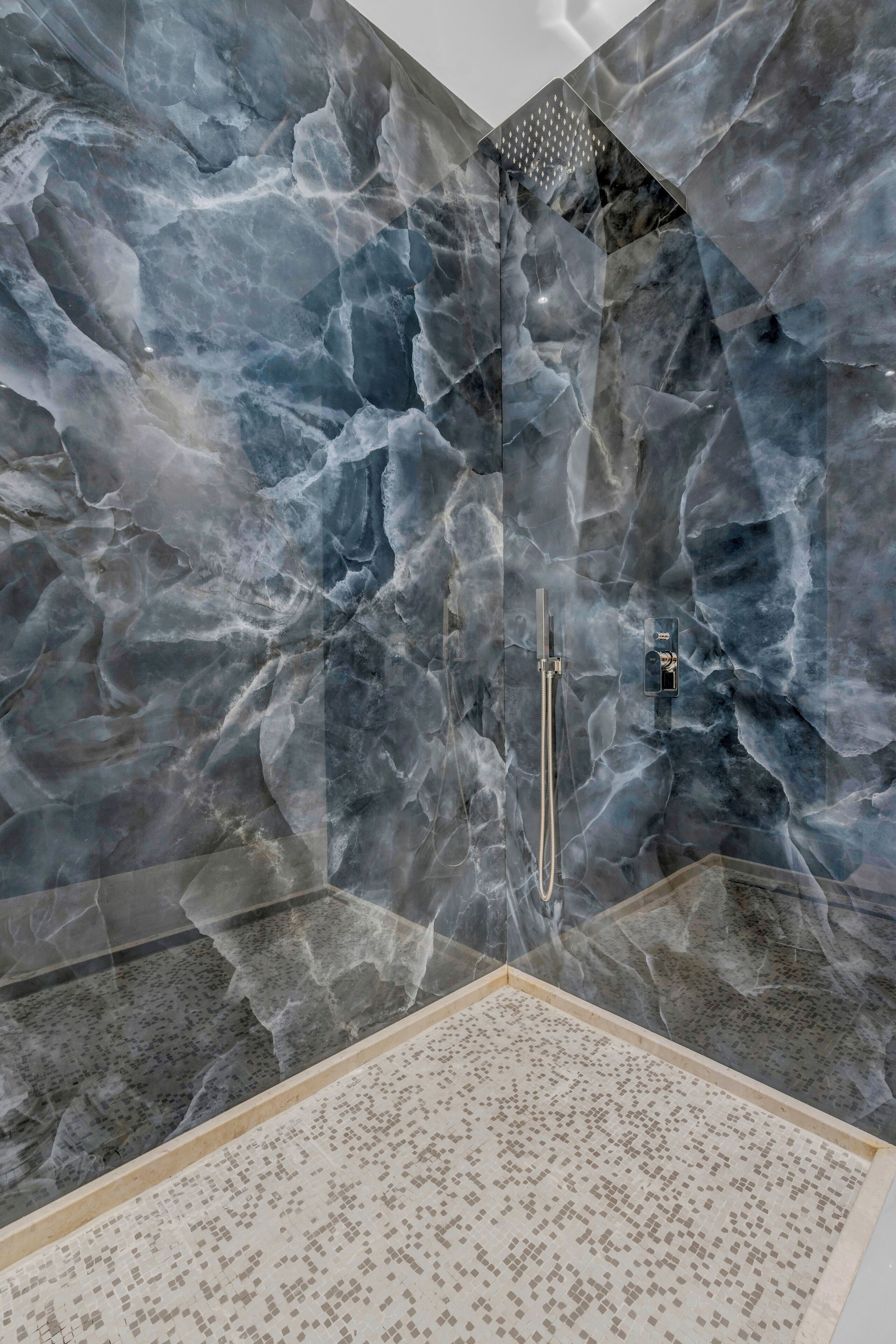 A bathroom with a marble wall, a shower, and a tiled floor.