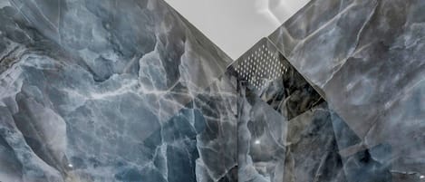 A bathroom with a marble wall, a shower, and a tiled floor.