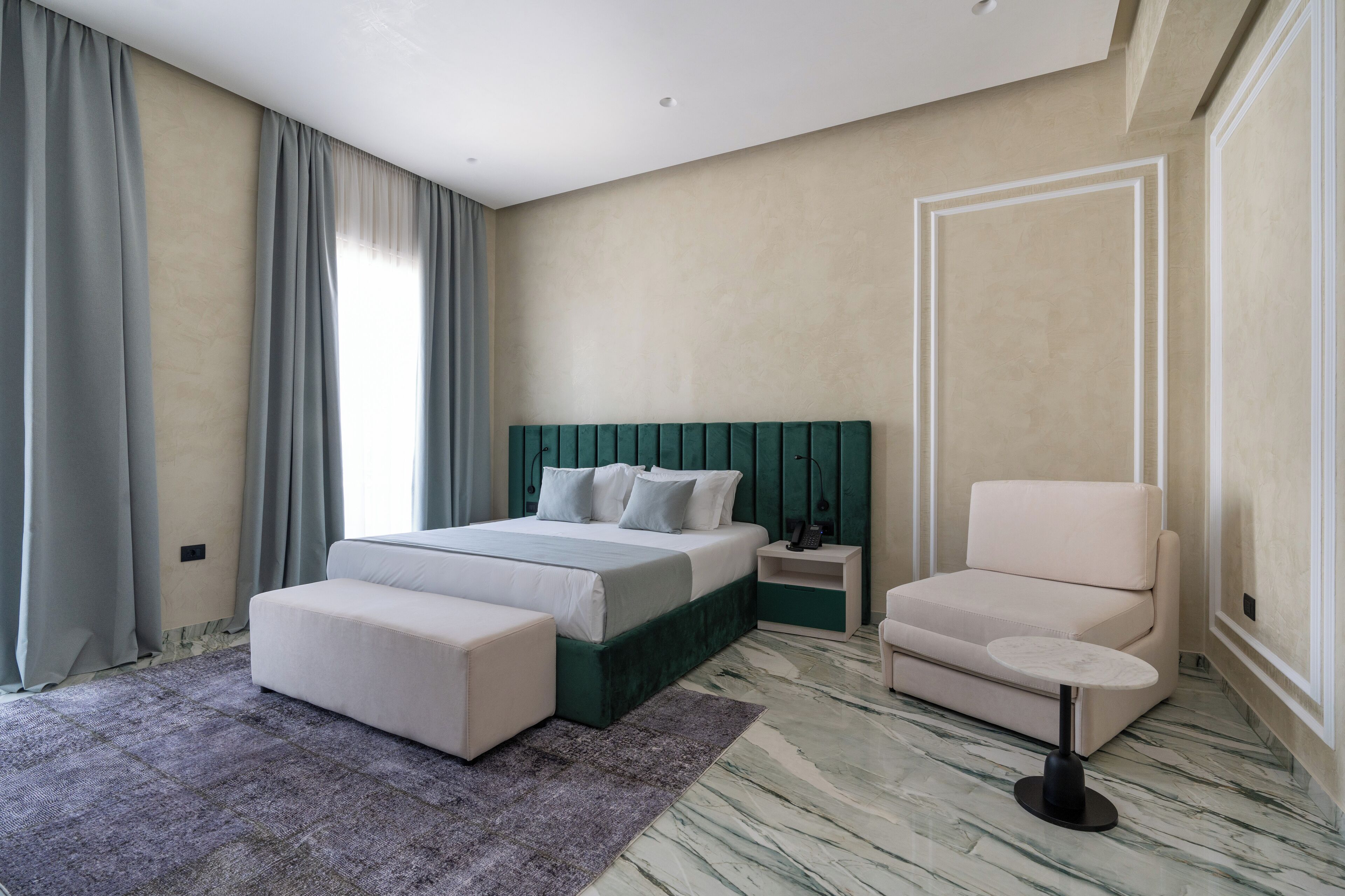 A modern bedroom with a bed, a chair, a small table, and a large window with curtains.
