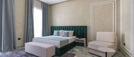 A modern bedroom with a bed, a chair, a small table, and a large window with curtains.