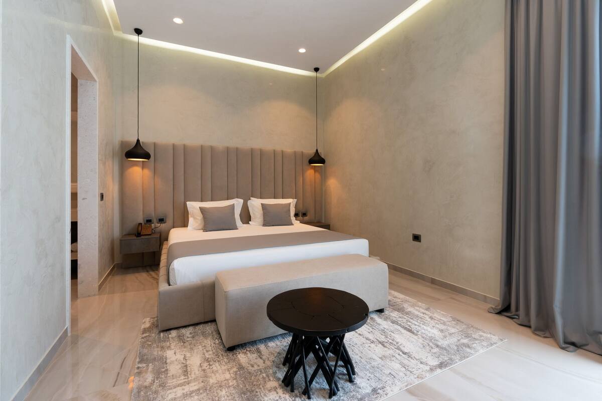 Un dormitorio moderno con una cama grande, mesitas de noche, una mesa redonda e iluminación ambiental.