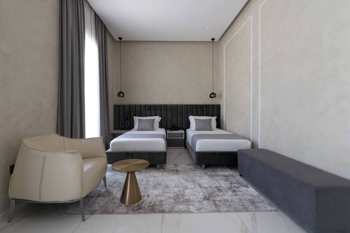 Una habitación de hotel moderna con dos camas, un sofá, una mesa de centro y un amplio ventanal con cortinas.