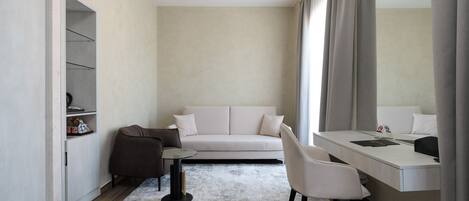 A modern hotel room with a sofa, a desk, a chair, a small table, and a wardrobe.