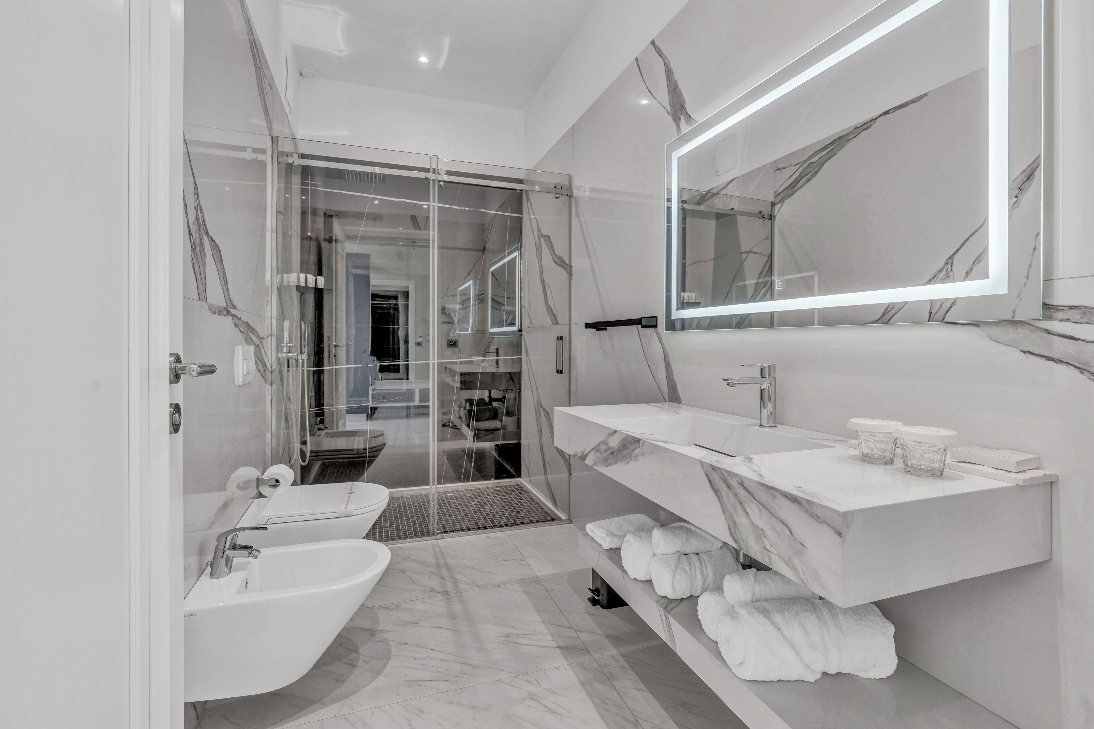 Un baño moderno con cabina de ducha de vidrio, tocador de mármol y un espejo grande.