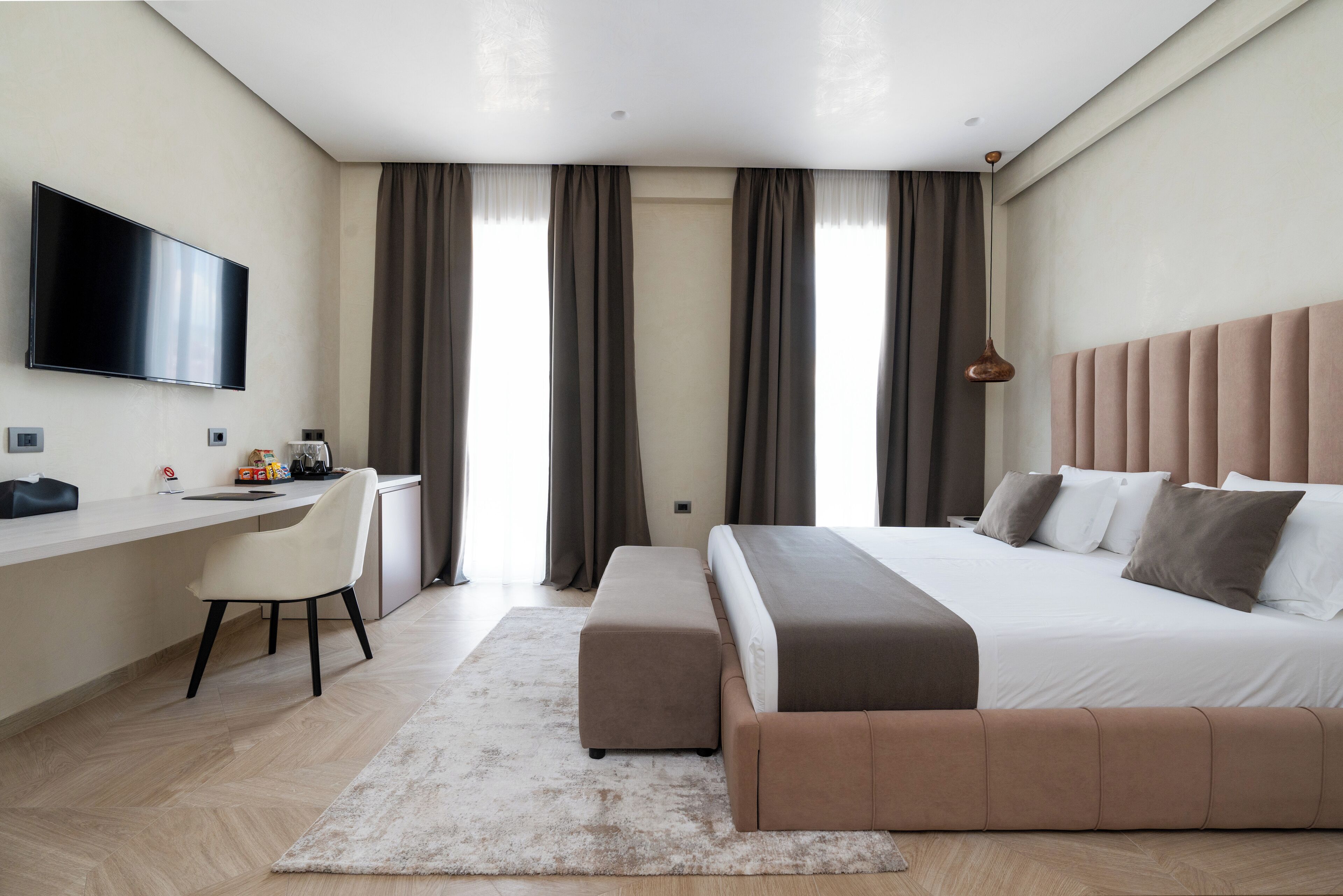 Une chambre d’hôtel moderne dotée d’un grand lit, d’un bureau avec une chaise, d’un téléviseur à écran plat et d’une grande fenêtre avec des rideaux.