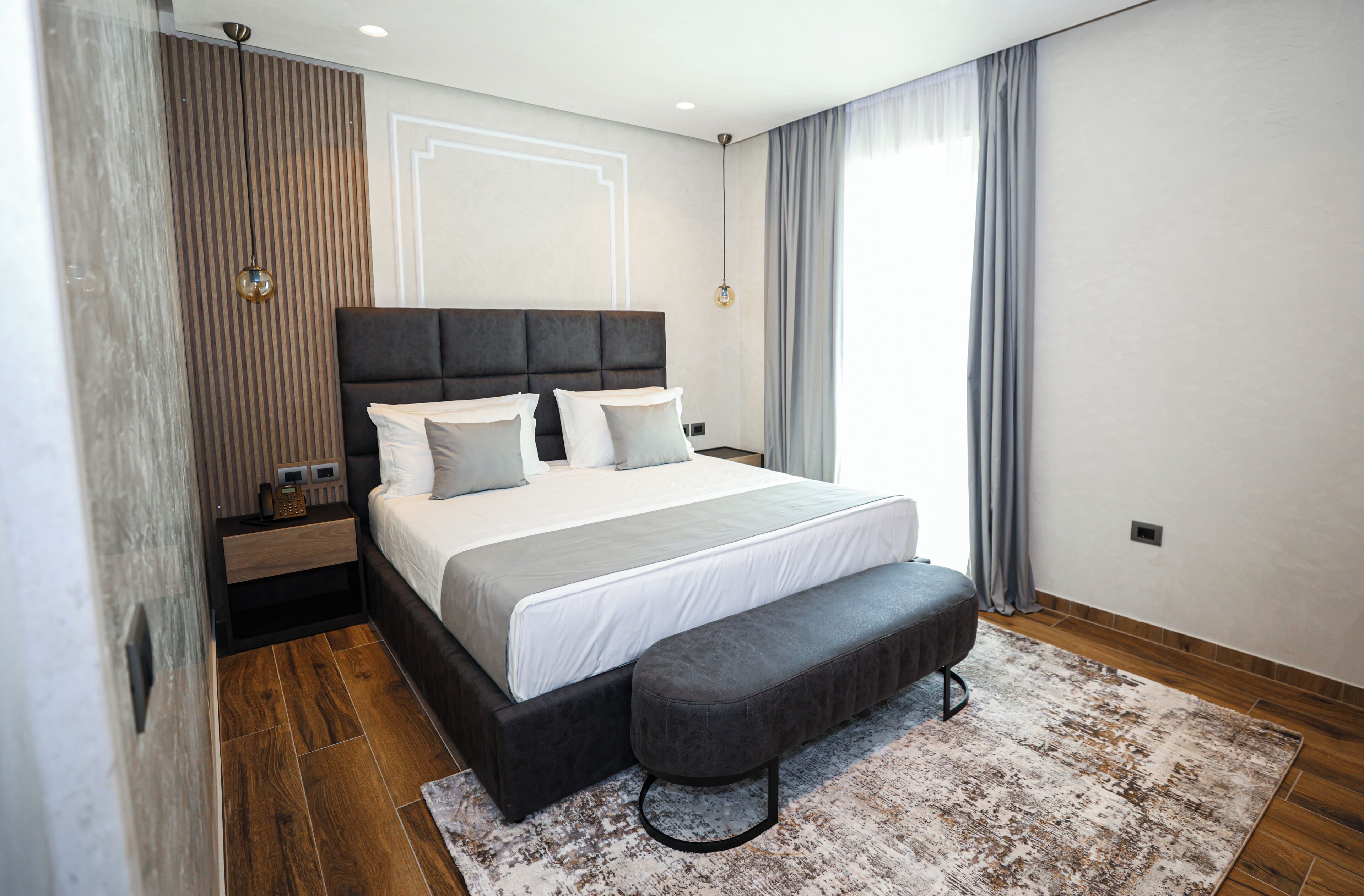 Un dormitorio moderno con una cama grande, un banco, paneles de madera y vistas al exterior.