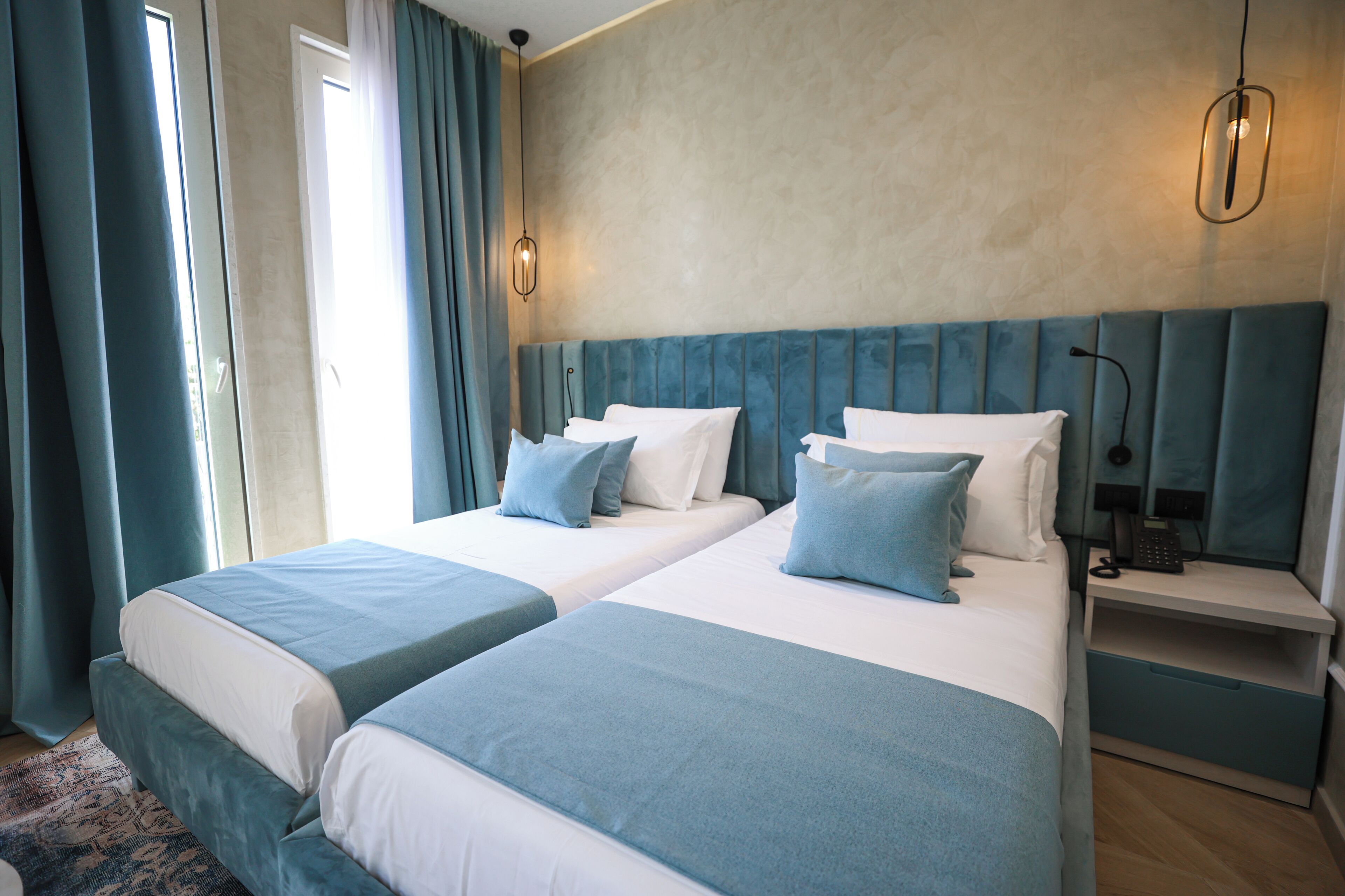 A hotel room with two beds, a nightstand, and a large window with curtains.