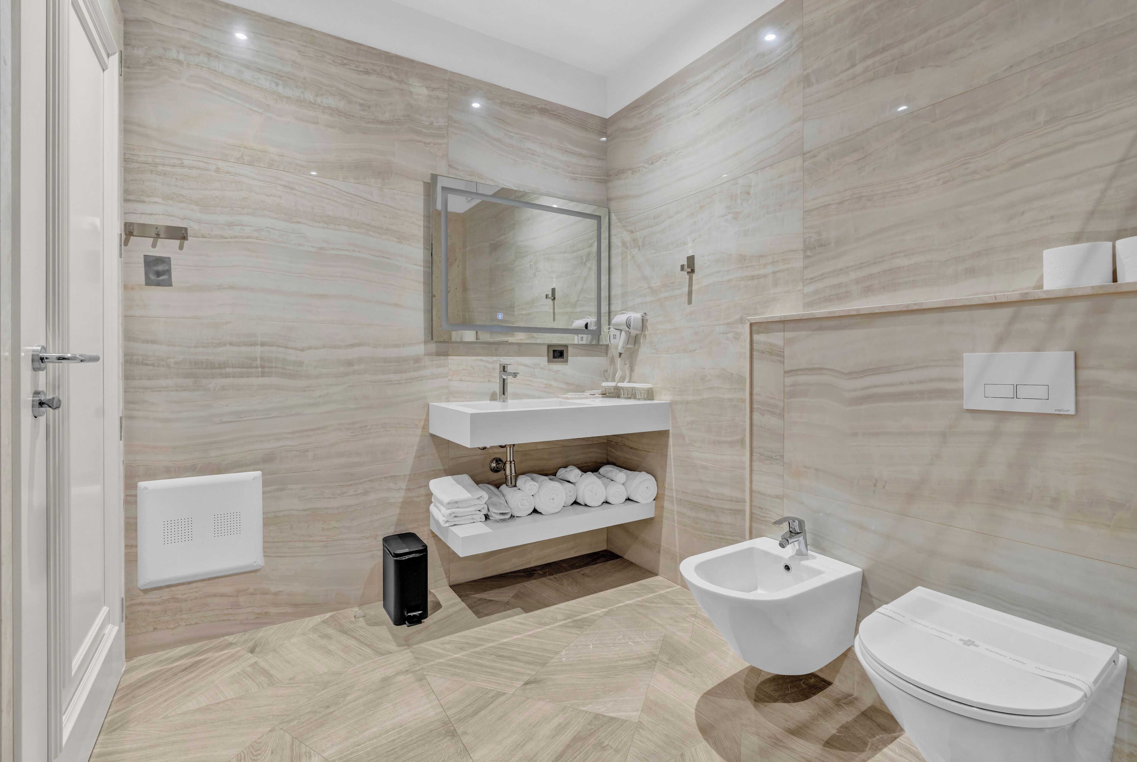 Un baño moderno con pared de mármol, lavamanos, un bidé y un inodoro.