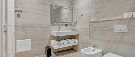 Un baño moderno con pared de mármol, lavamanos, un bidé y un inodoro.