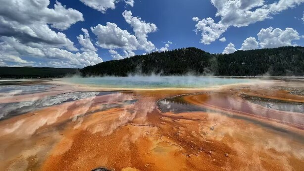 Ein weiter Blick über eine geothermische Gegend mit mineralreichem Wasser und einem bewaldeten Berg im Hintergrund.