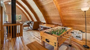 Ein gemütliches Loft mit Holzbalkendecke, einem Kicker, einer Couch und einer Lampe.