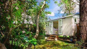 A small, white mobile home with a glass door, surrounded by lush greenery and trees. - Beautiful Shepherds Hut B&B nr Stonehenge, Avebury, Salisbury, Bath - WiFi, TV (Haxton)