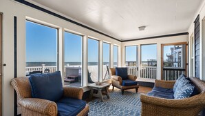 Un balcón soleado con mobiliario de mimbre, ventanas amplias y vista al mar.