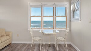 Una habitación con una mesa redonda y dos sillas de mimbre frente a un ventanal con vista al océano.