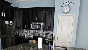 A modern kitchen with dark cabinets, a granite countertop, and a central island with bar stools. - Ground level condo near beach with a deck, washer/dryer AC & Pool (Corpus Christi)