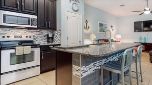 A modern kitchen with dark cabinets, stainless steel appliances, a tiled backsplash, and a granite countertop. - Ground level condo near beach with a deck, washer/dryer AC & Pool (Corpus Christi)