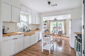 Moderni keittiö, jossa on valkoiset kaapit, puinen työtaso sekä ruokailutila pöytineen ja tuoleineen.